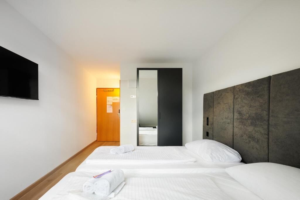 Een hotelkamer met twee bedden, een wandtelevisie en een houten vloer.