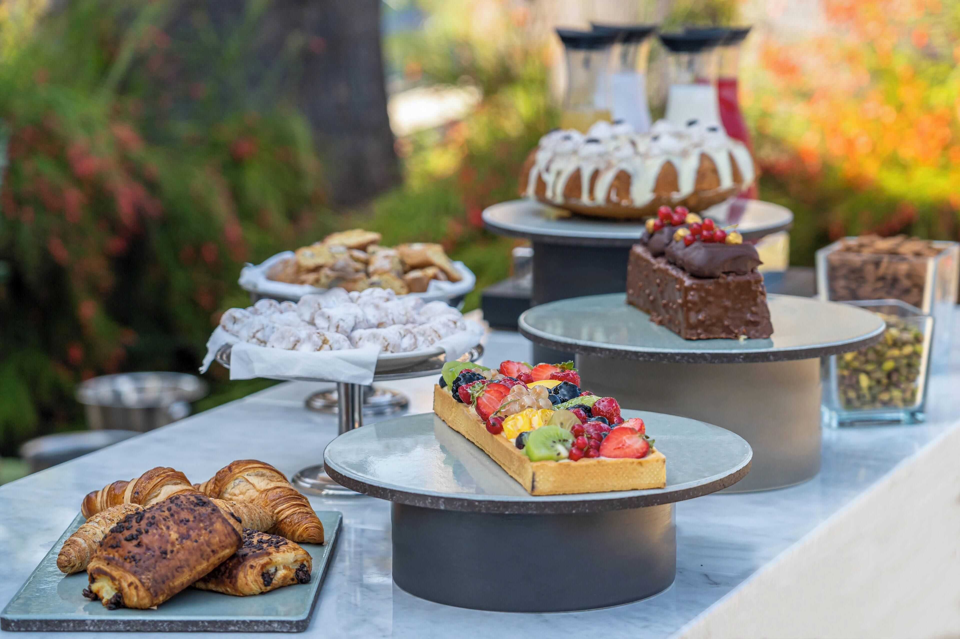 Un bufé con diversos pasteles y postres, incluyendo croissants, una tarta de fruta y un pastel de chocolate.