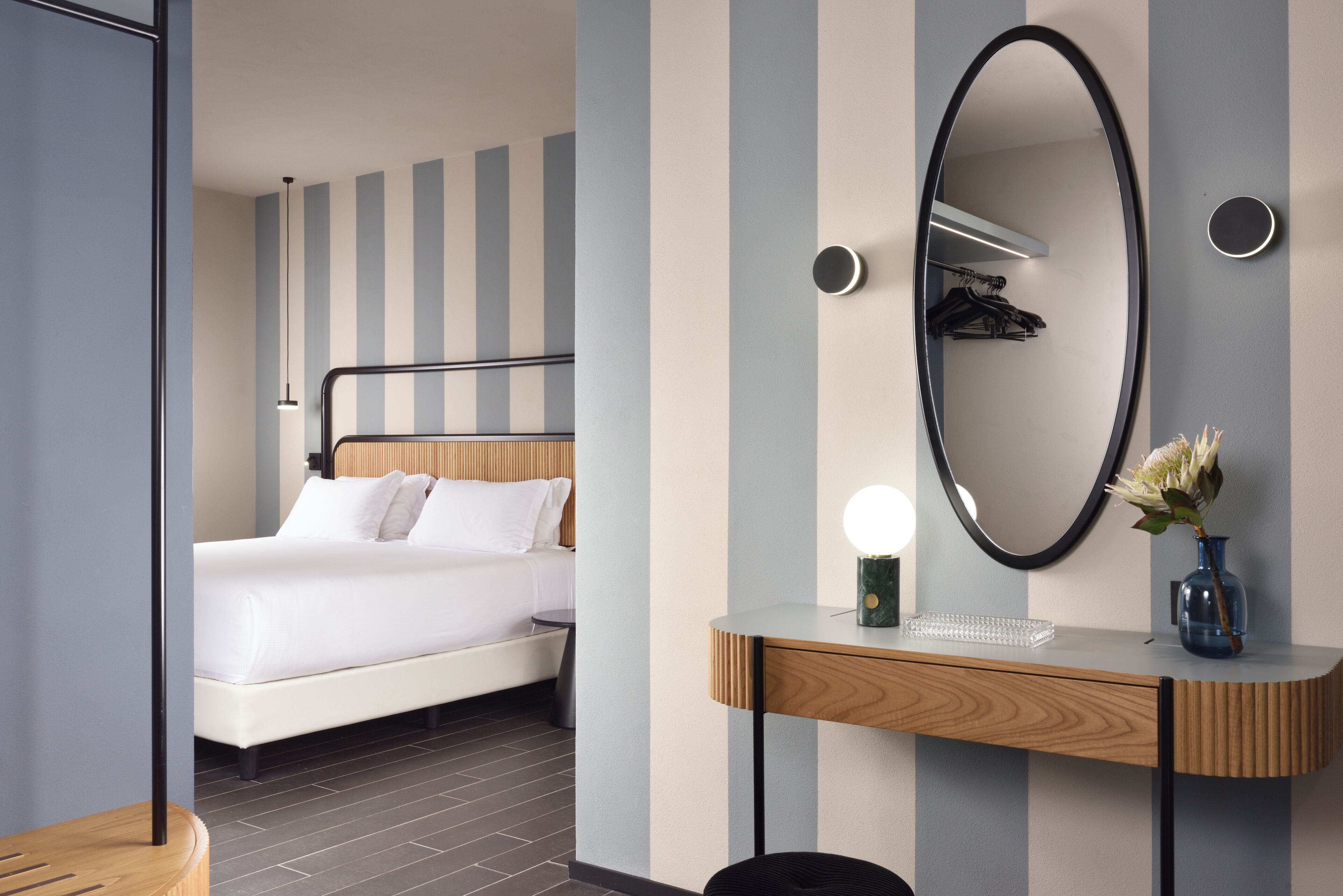 A modern hotel room with a bed, a vanity with a mirror, and a desk.