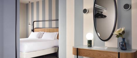 A modern hotel room with a bed, a vanity with a mirror, and a desk.