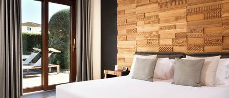 A bedroom with a large bed, a wooden headboard with intricate carvings, a bedside table with a lamp, and a view of an outdoor pool area through a sliding glass door.