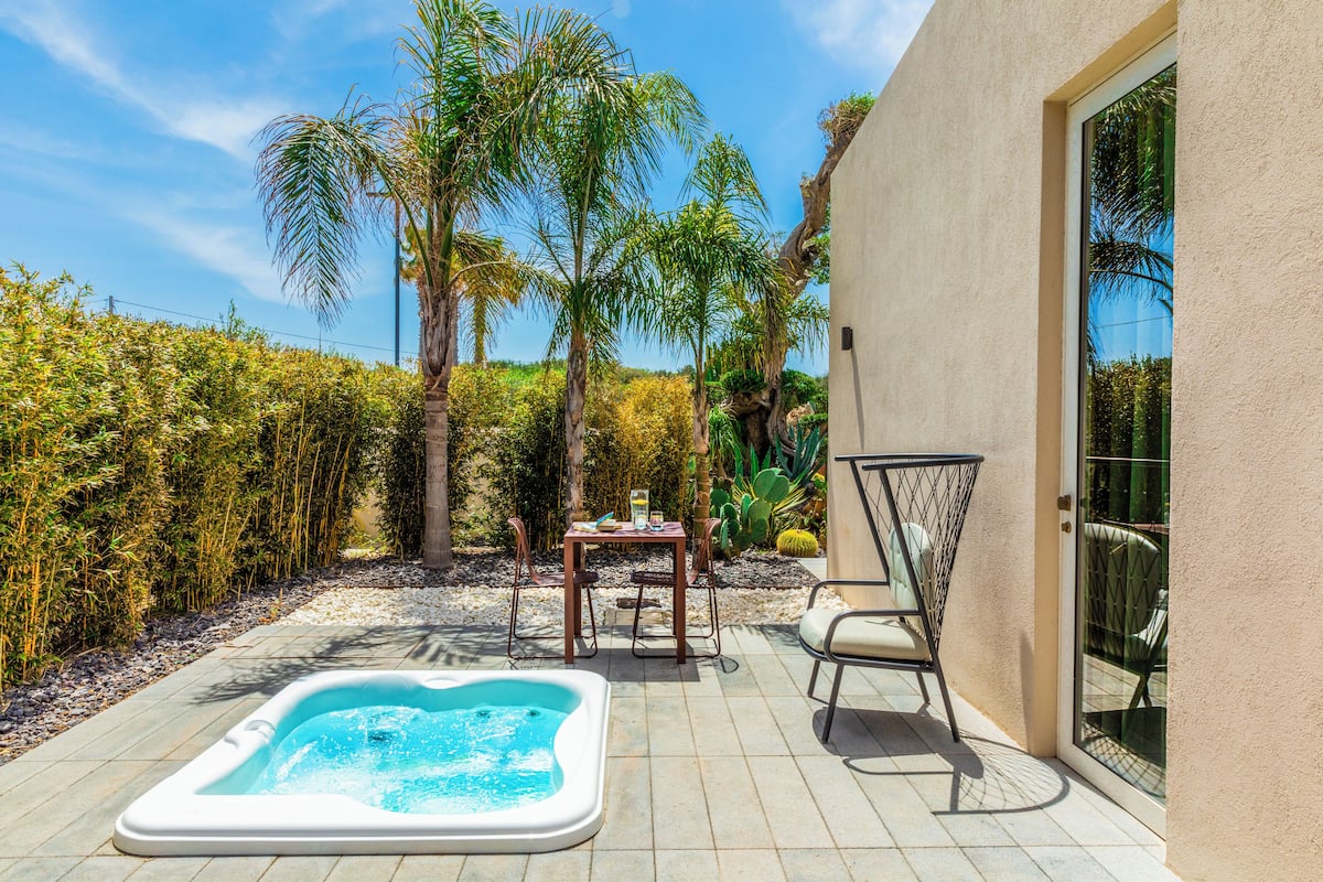A patio with a hot tub, a table, chairs, and a glass door leading to a balcony.