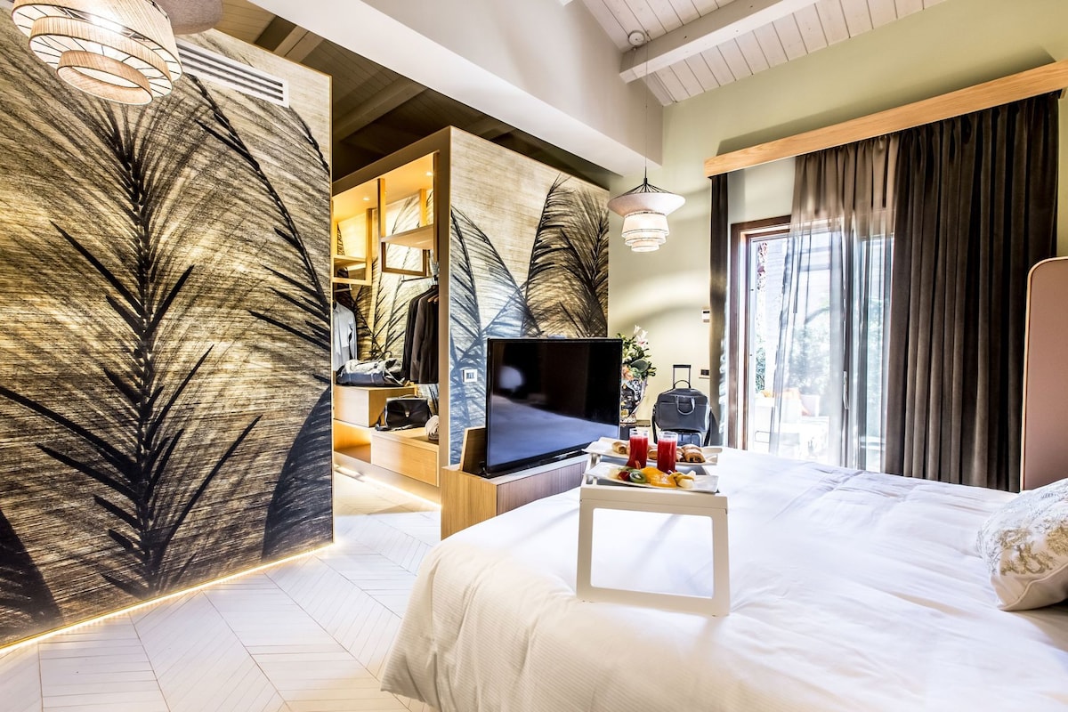 A hotel room with a bed, a TV, a tray with breakfast, and a large leaf-patterned wall.