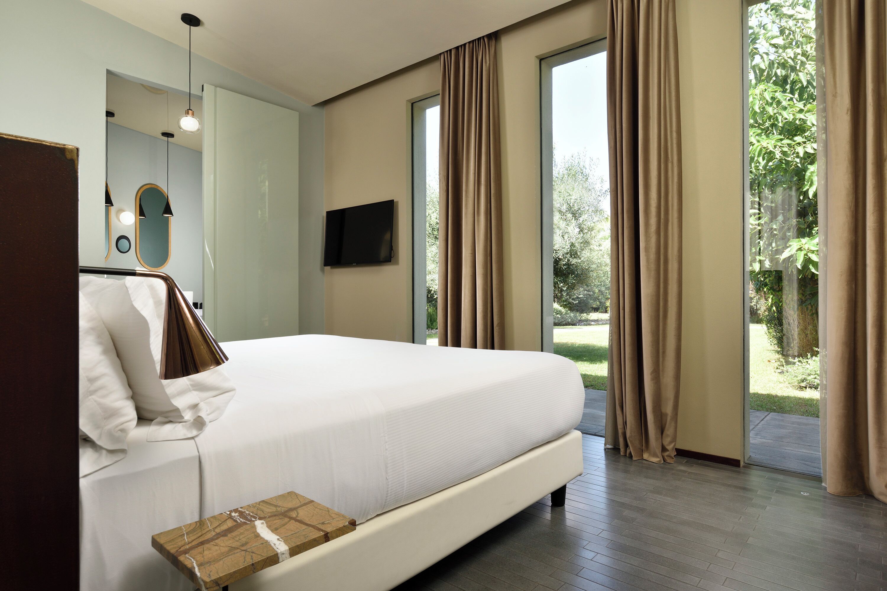 A bedroom with a large bed, a bedside table, a TV, and a view of the outdoors.