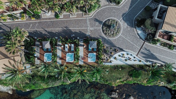 An aerial view of a resort with multiple swimming pools, palm trees, and a clear view of the coastline.