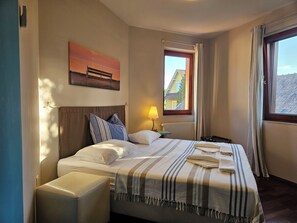 Une chambre d’hôtel avec un lit, une fenêtre avec des rideaux, une table de chevet, une lampe et un tableau au mur.