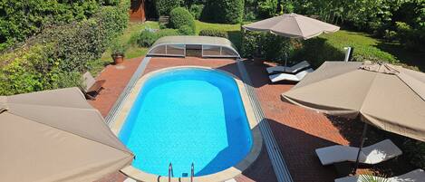 A rectangular swimming pool with a tiled edge, surrounded by a brick patio. There are lounge chairs and umbrellas around the pool area.
