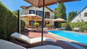 Ein Poolbereich mit Liegestühlen und Sonnenschirmen, ein Schwimmbecken und ein Gebäude mit einem Balkon.