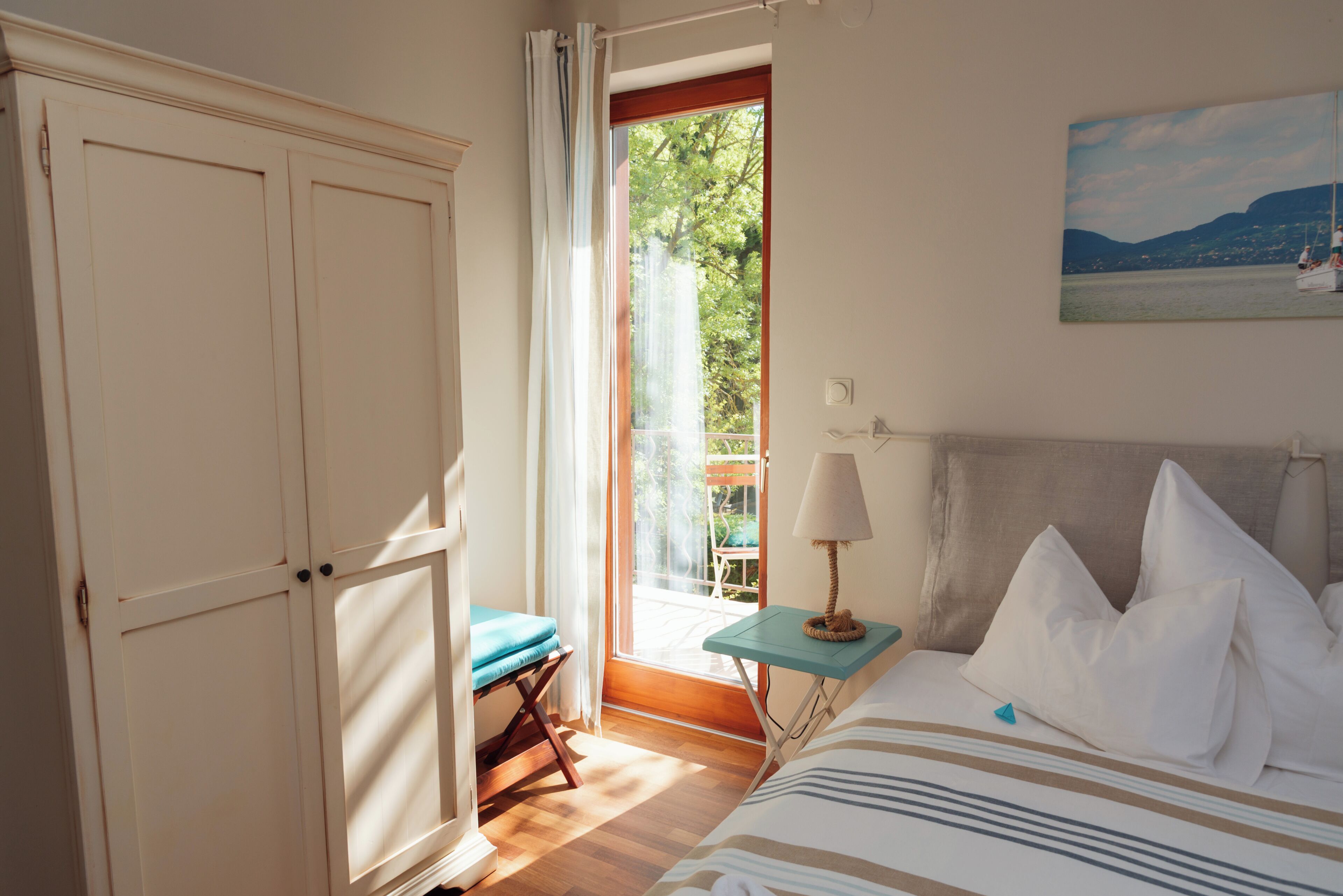 A bedroom with a bed, a nightstand, a window with a view of greenery, and a door.