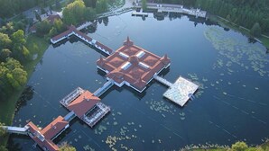 Eine Vogelperspektive auf ein großes, kreisförmiges Gewässer mit einer zentralen Insel, die traditionelle Architektur mit mehreren Dächern und verbundenen Gängen aufweist.