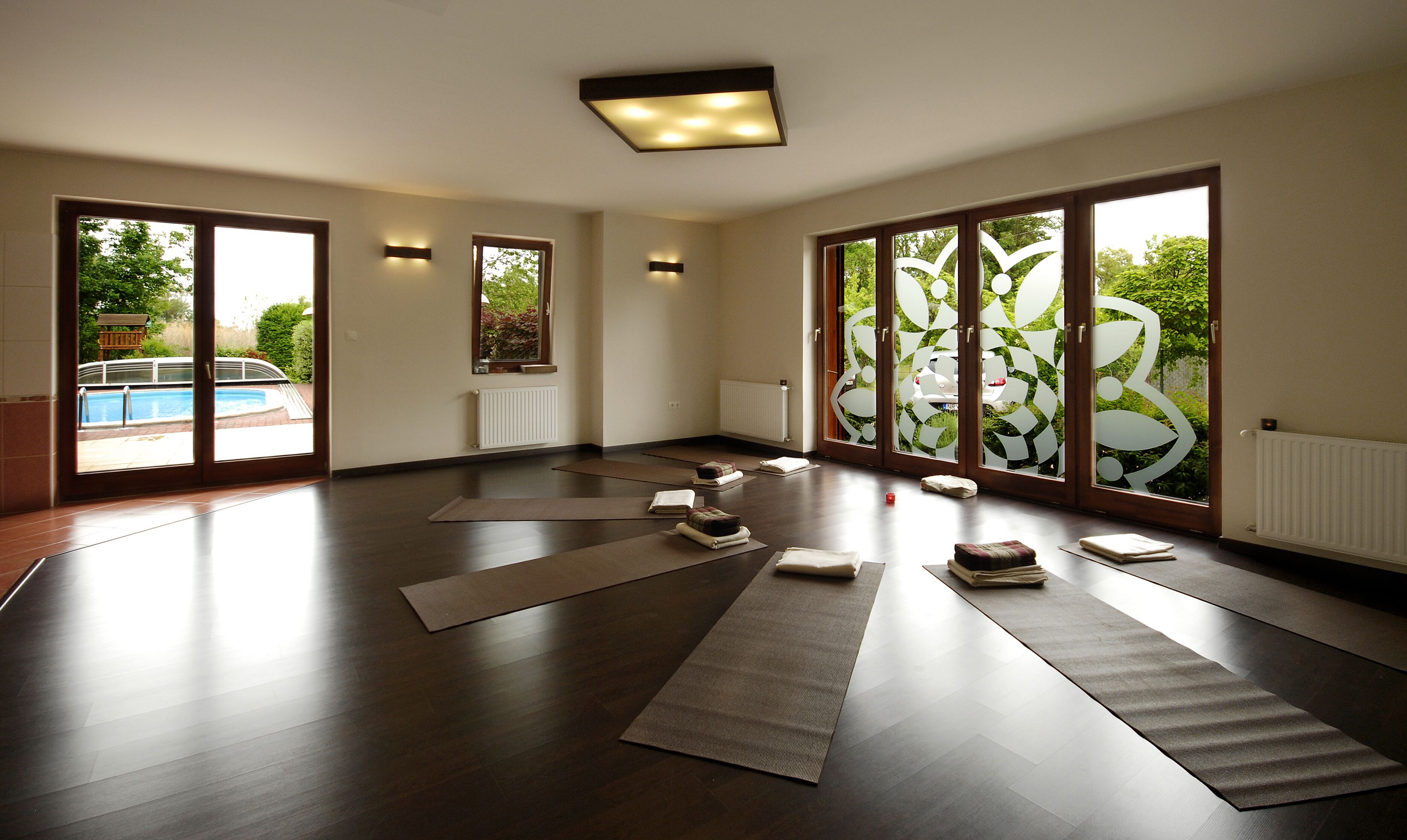 A spacious room with large sliding glass doors, a view of a swimming pool, and a ceiling light fixture.