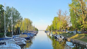 Ein ruhiger Kanal mit vertäuten Booten an beiden Ufern, umgeben von Bäumen und einem klaren Himmel.