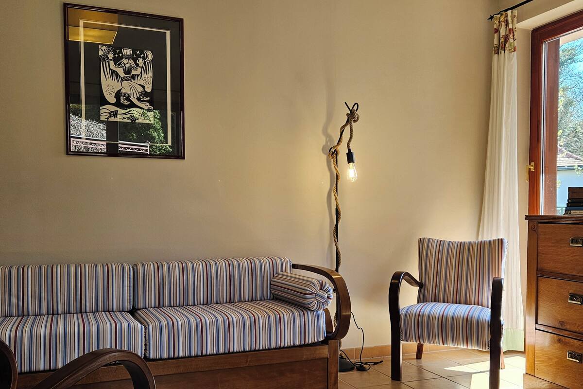 A room with a striped sofa, a chair, a wooden cabinet, and a framed picture on the wall.