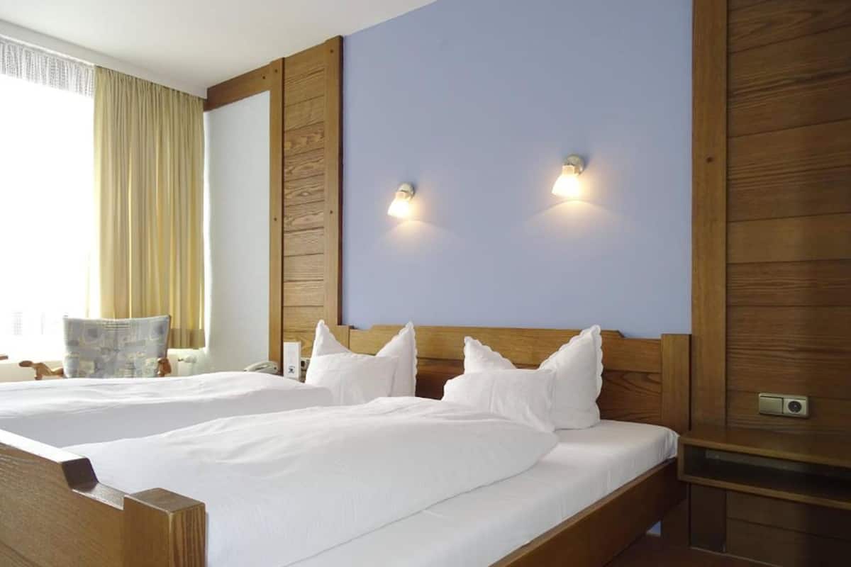 A hotel room with two beds, wooden headboards, and a large window with curtains.