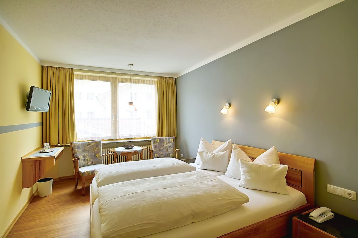 A hotel room with two beds, a desk, a chair, a television, and a window with curtains.
