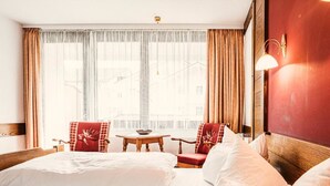 A hotel room with a bed, two armchairs, a small table, and a window with curtains. - Jakob (Fuessen)