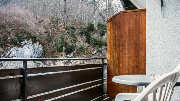 A balcony with a wooden railing, a small table, and a white chair. - Jakob (Fuessen)
