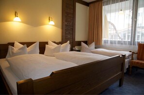 A hotel room with two wooden beds, a chair, and a large window with curtains. - Jakob (Fuessen)
