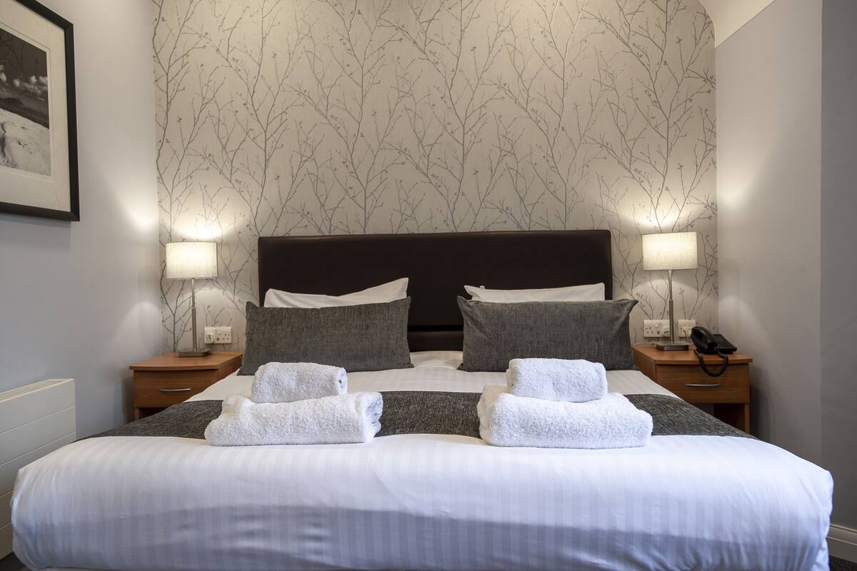 A neatly made bed with white linens and gray pillows, two bedside lamps, and a framed picture on the wall.