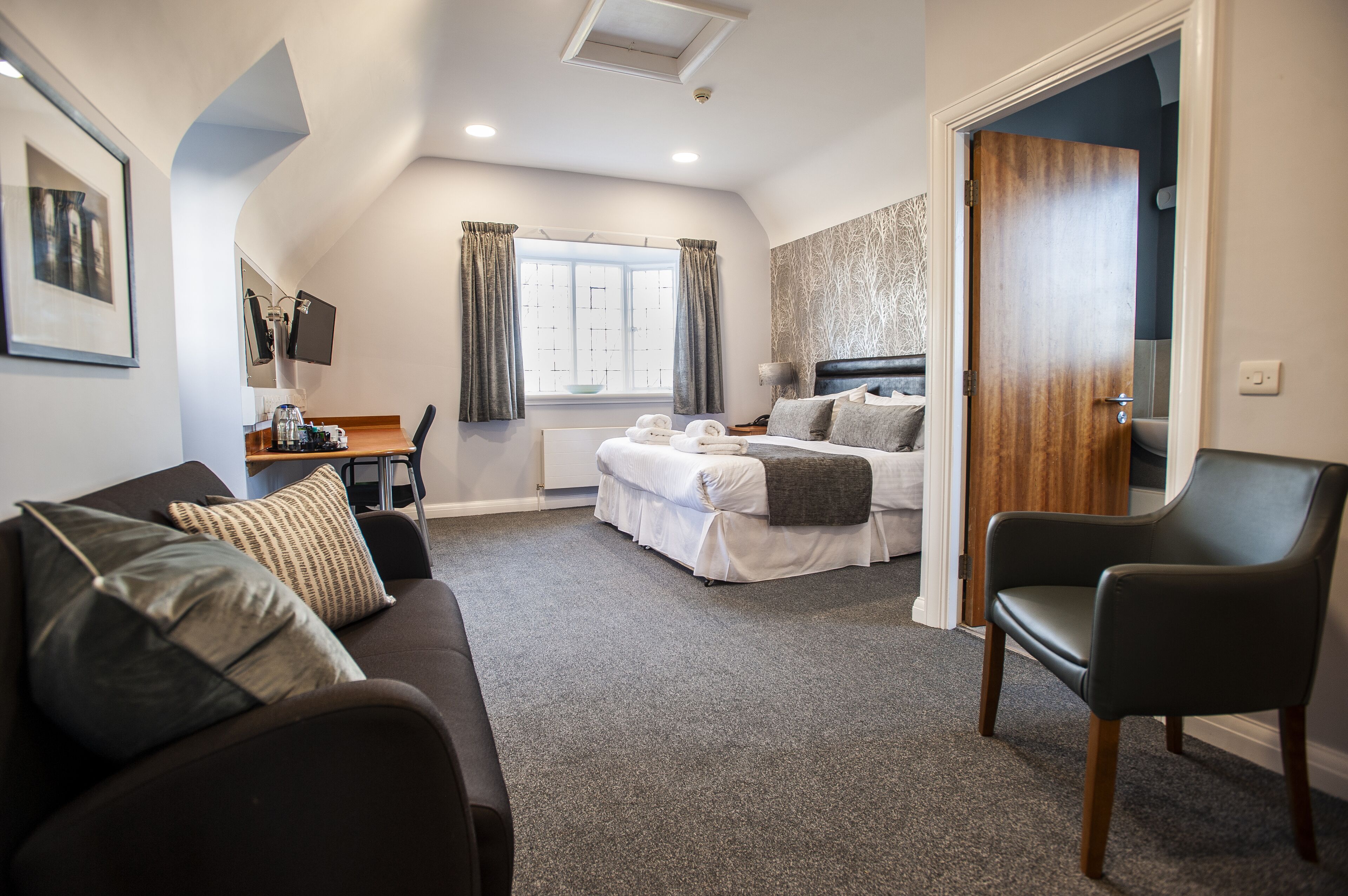 Una habitación de hotel moderna con cama, sofá, sillón, escritorio y ventana con cortinas.