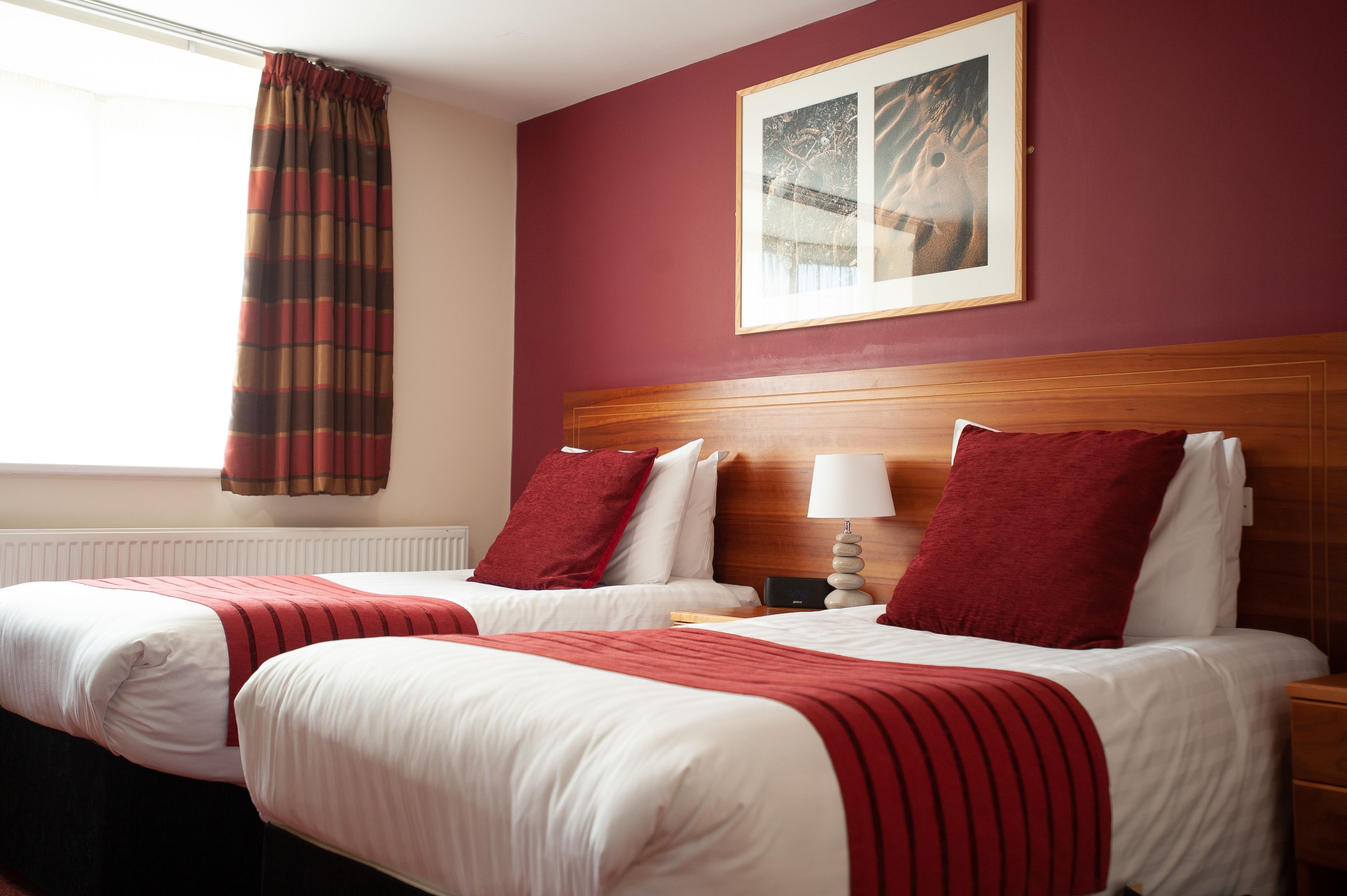 A hotel room with two beds, a wooden headboard, a framed picture on the wall, and a window with a curtain.