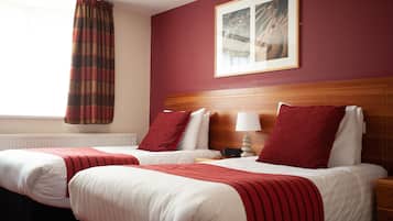 A hotel room with two beds, a wooden headboard, a framed picture on the wall, and a window with a curtain.