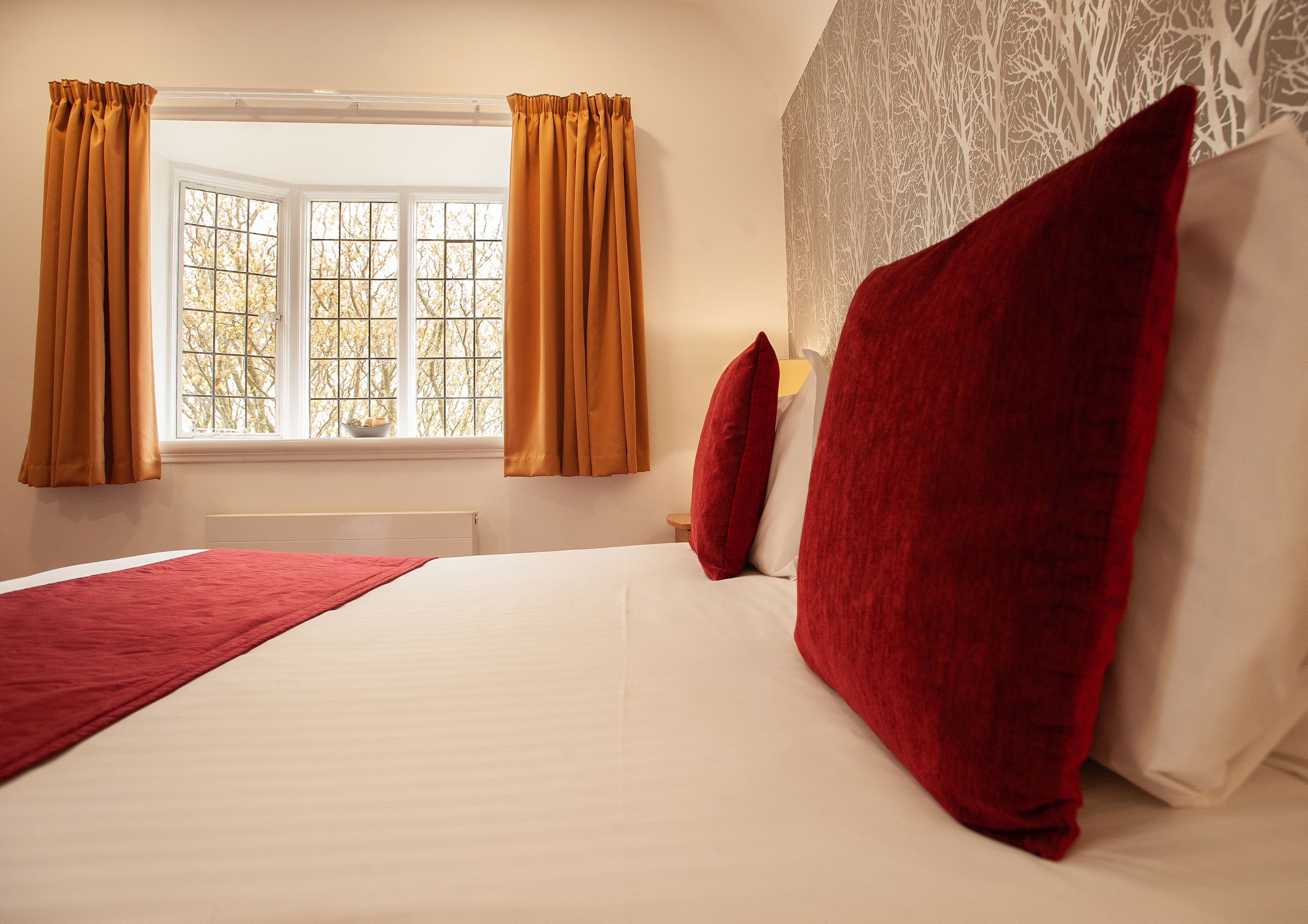 A bedroom with a large bed, red pillows, and curtains.