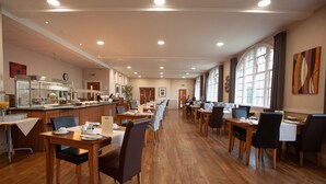 Un comedor amplio con varias mesas y sillas, un mostrador de buffet y grandes ventanales que dejan entrar luz natural.