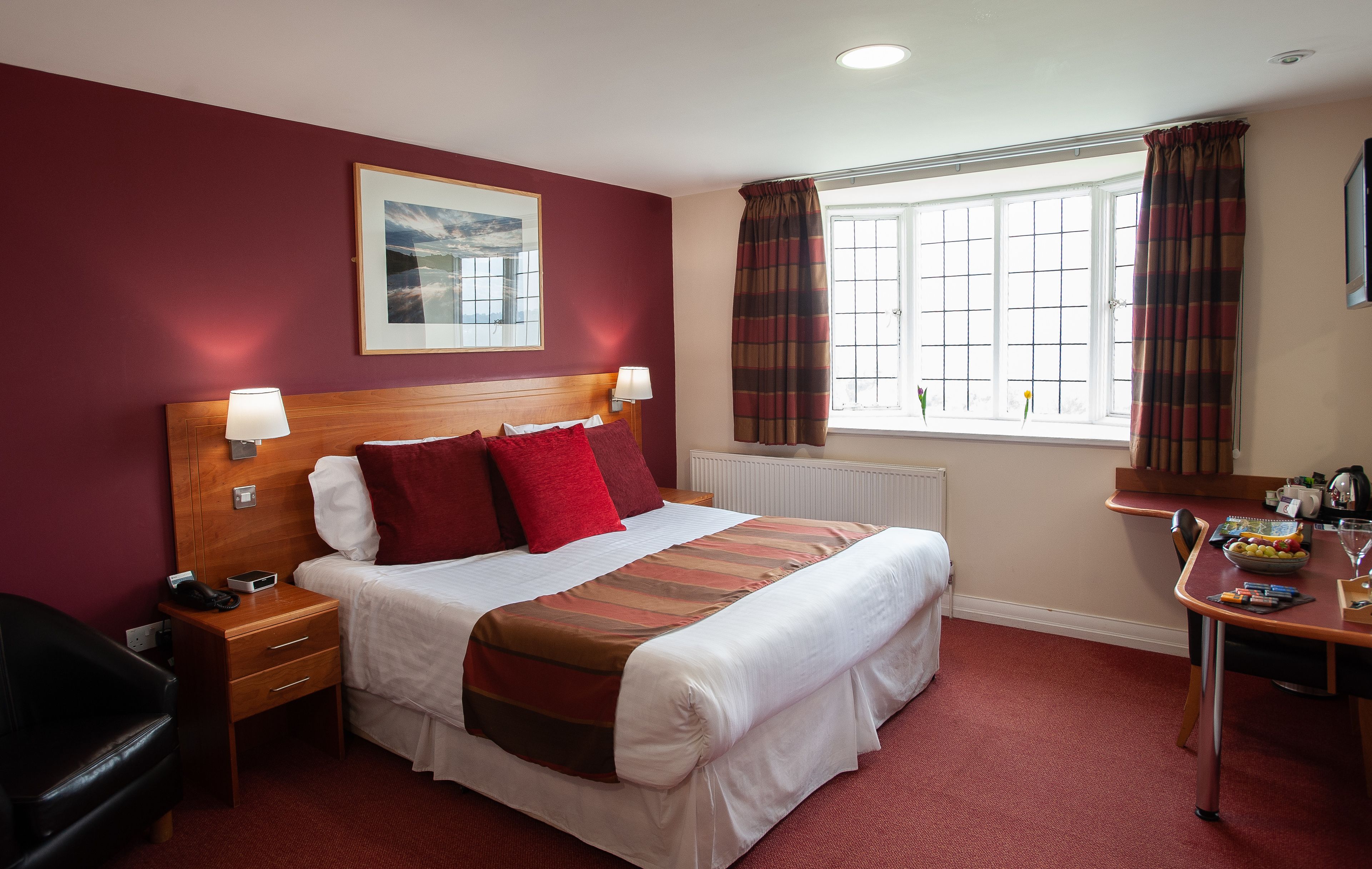 A hotel room with a large bed, bedside tables, a desk with a chair, and a window with curtains.