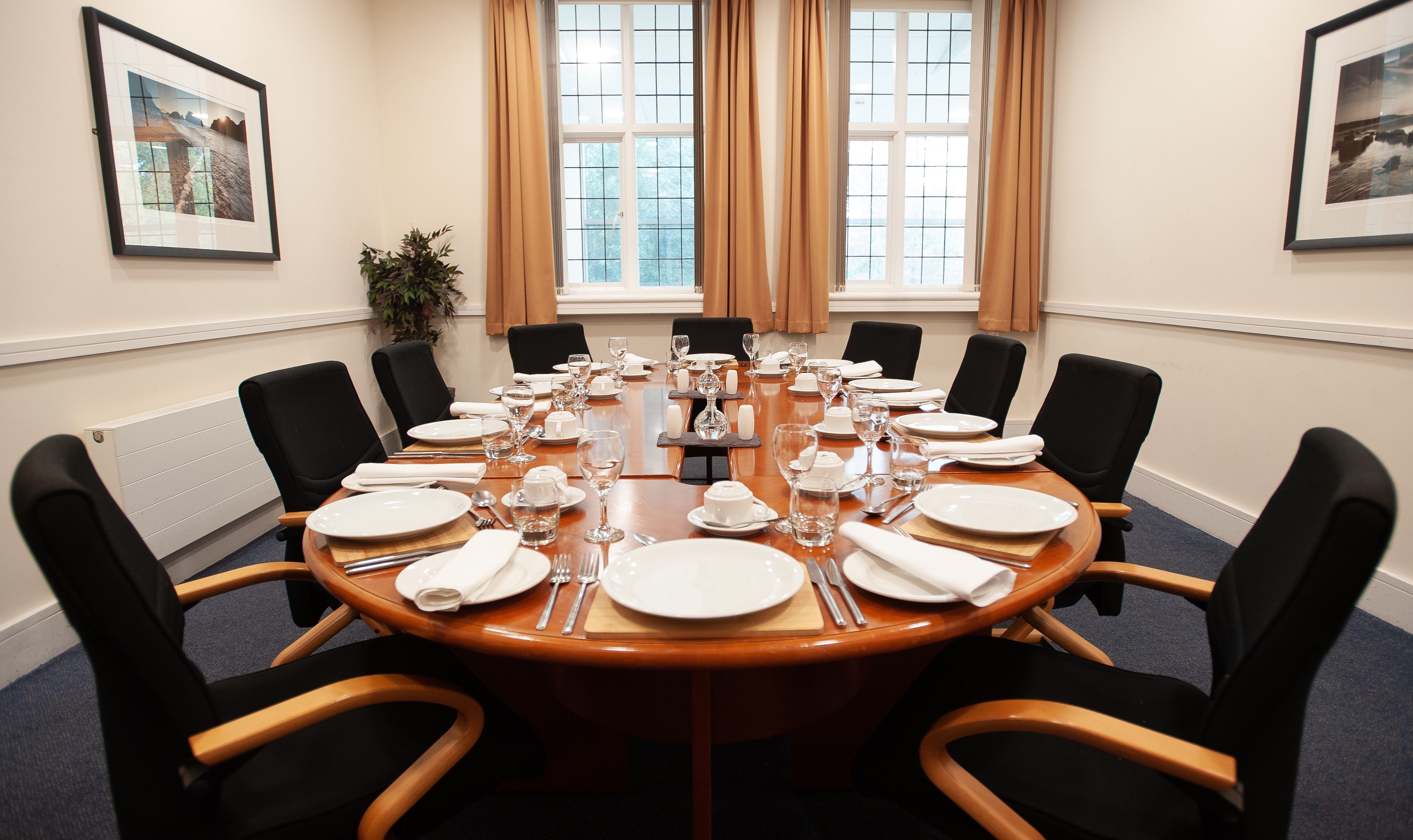 Un salón de conferencias con una mesa redonda dispuesta para una reunión, equipado con sillas, platos, vasos y cubiertos.