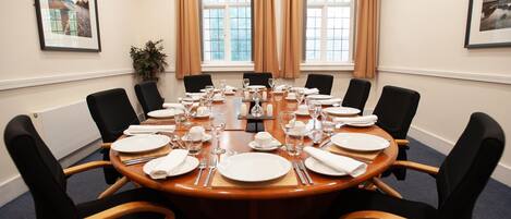 A conference room with a round table set for a meeting, equipped with chairs, plates, glasses, and cutlery.