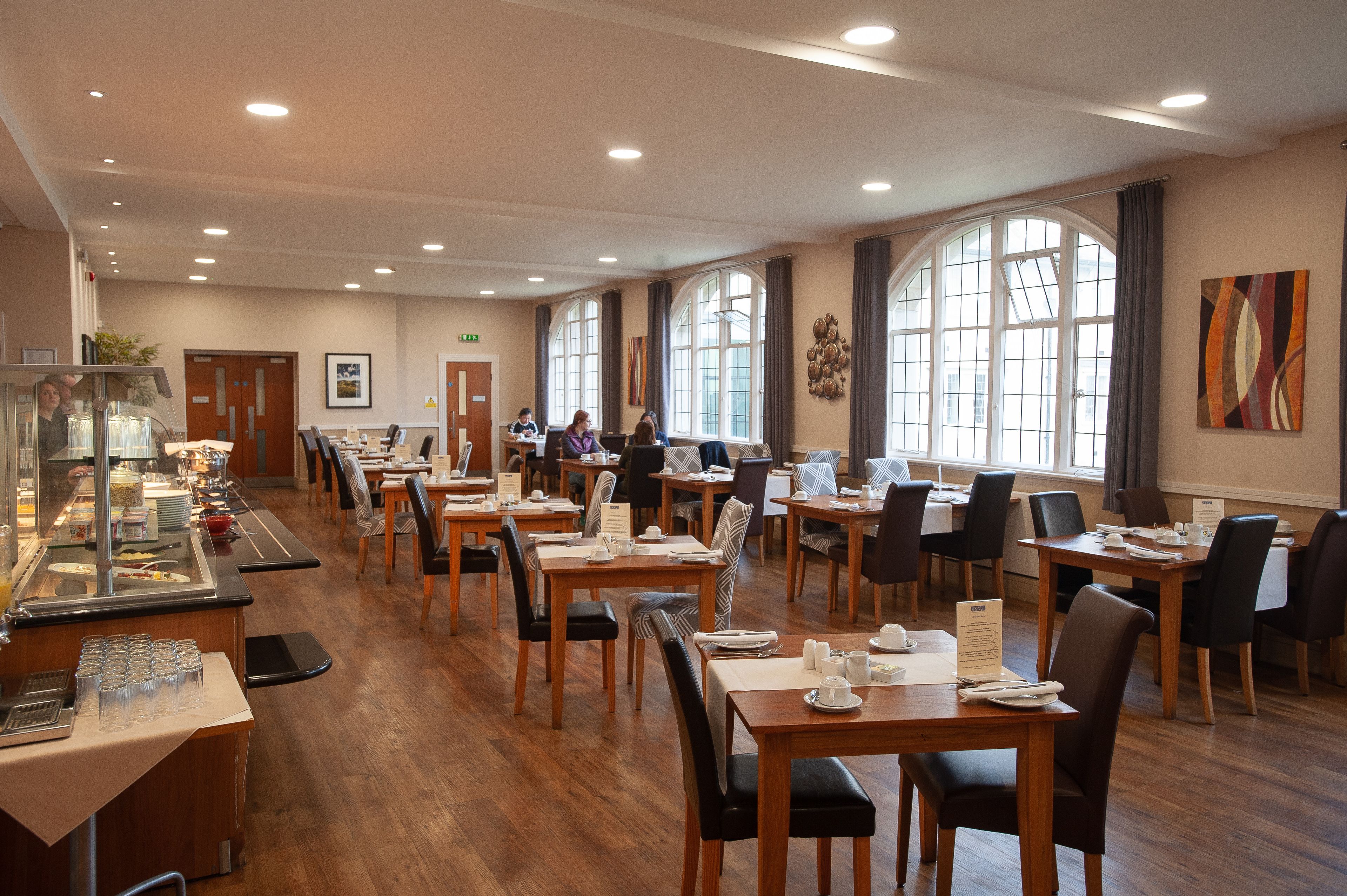 Un comedor amplio con varias mesas y sillas, ventanas grandes y un mostrador tipo buffet.