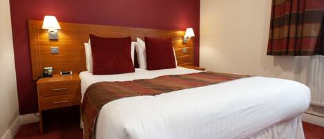 Una habitación de hotel con una cama grande, dos mesitas de noche y un cabecero con iluminación integrada.