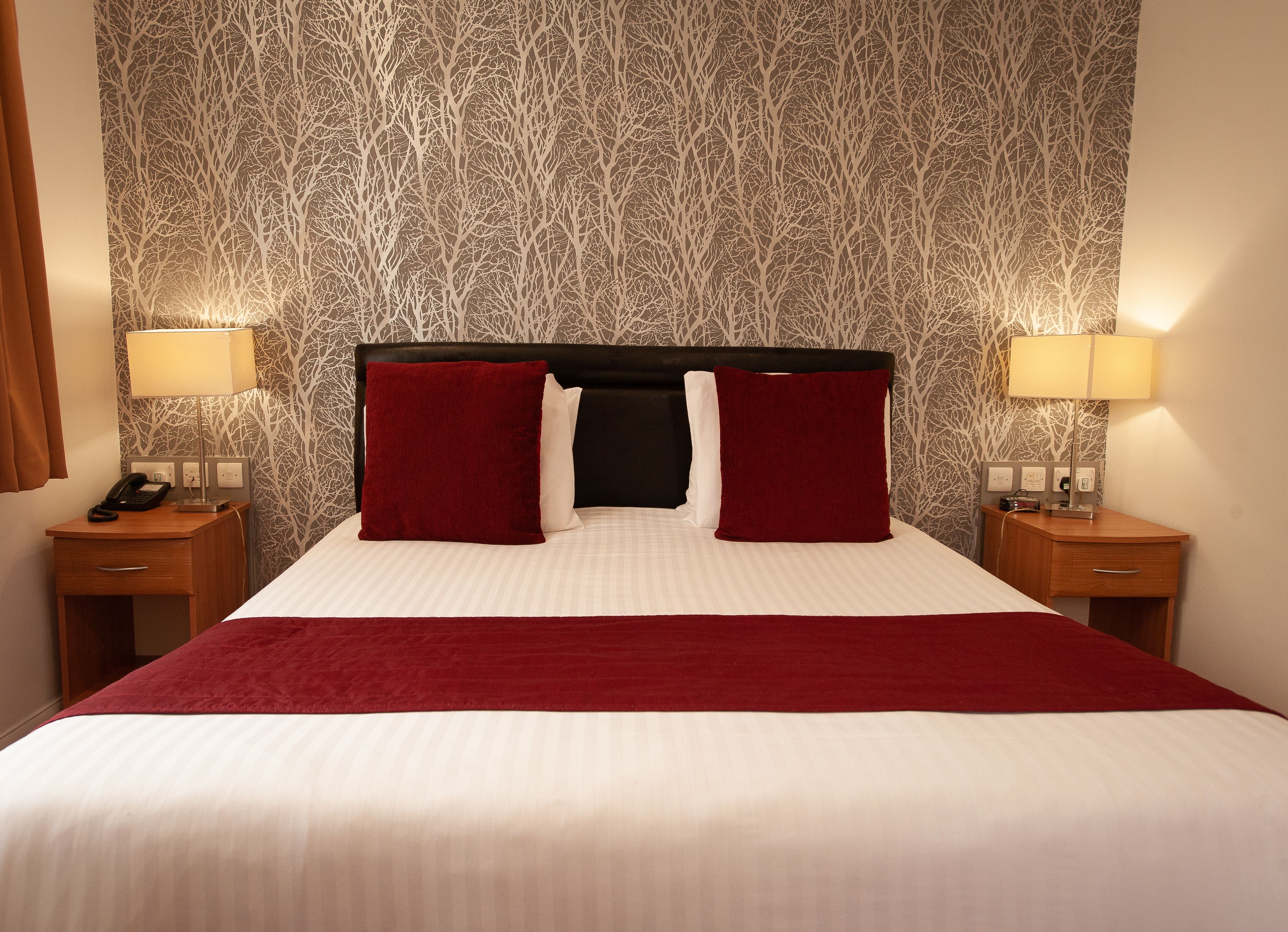 Ein Hotelzimmer mit einem großen Bett, zwei Nachttischen, einer Lampe und einem Telefon.