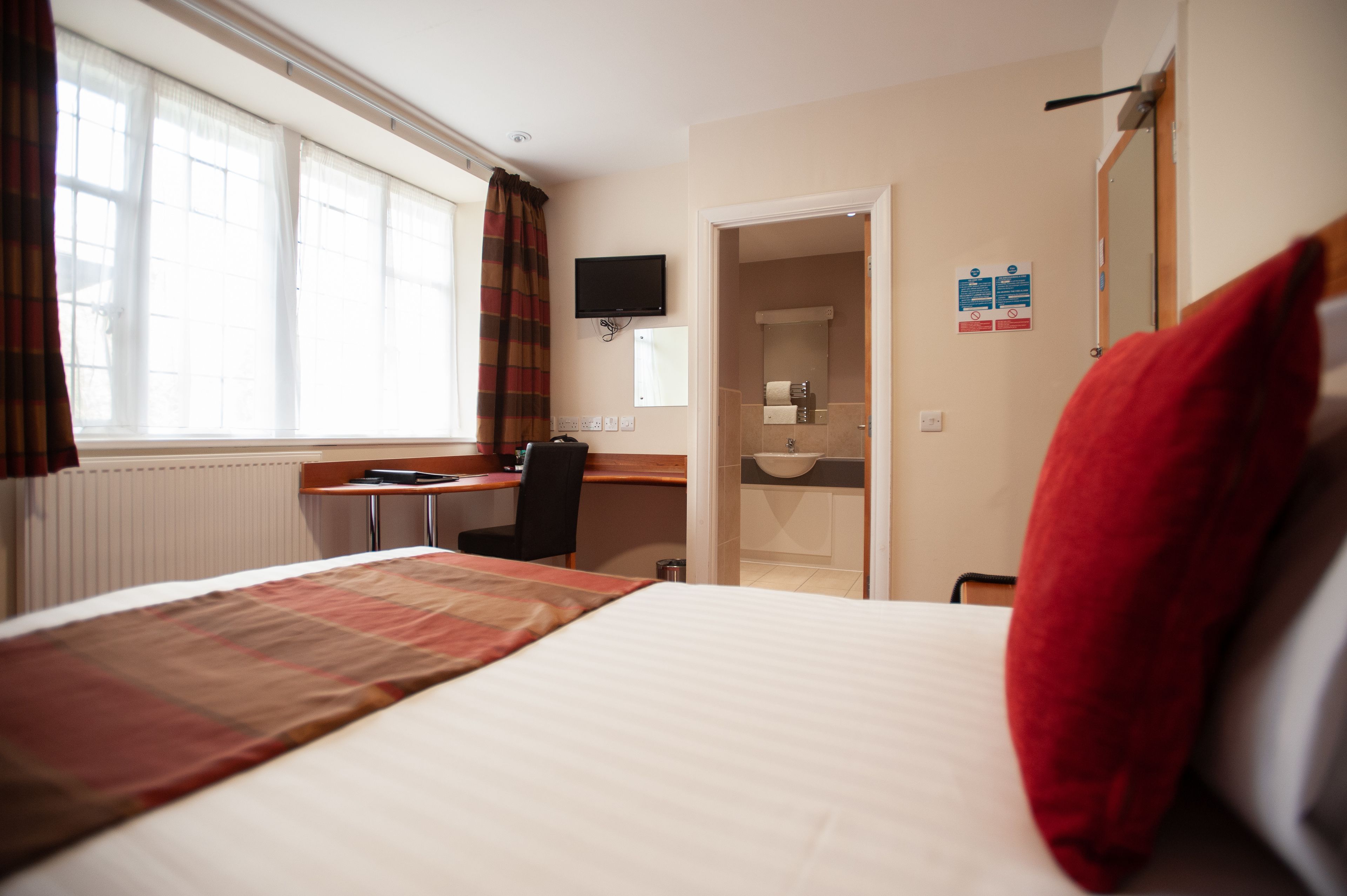 A hotel room with a bed, a desk, a chair, a television, and a bathroom visible through an open door.