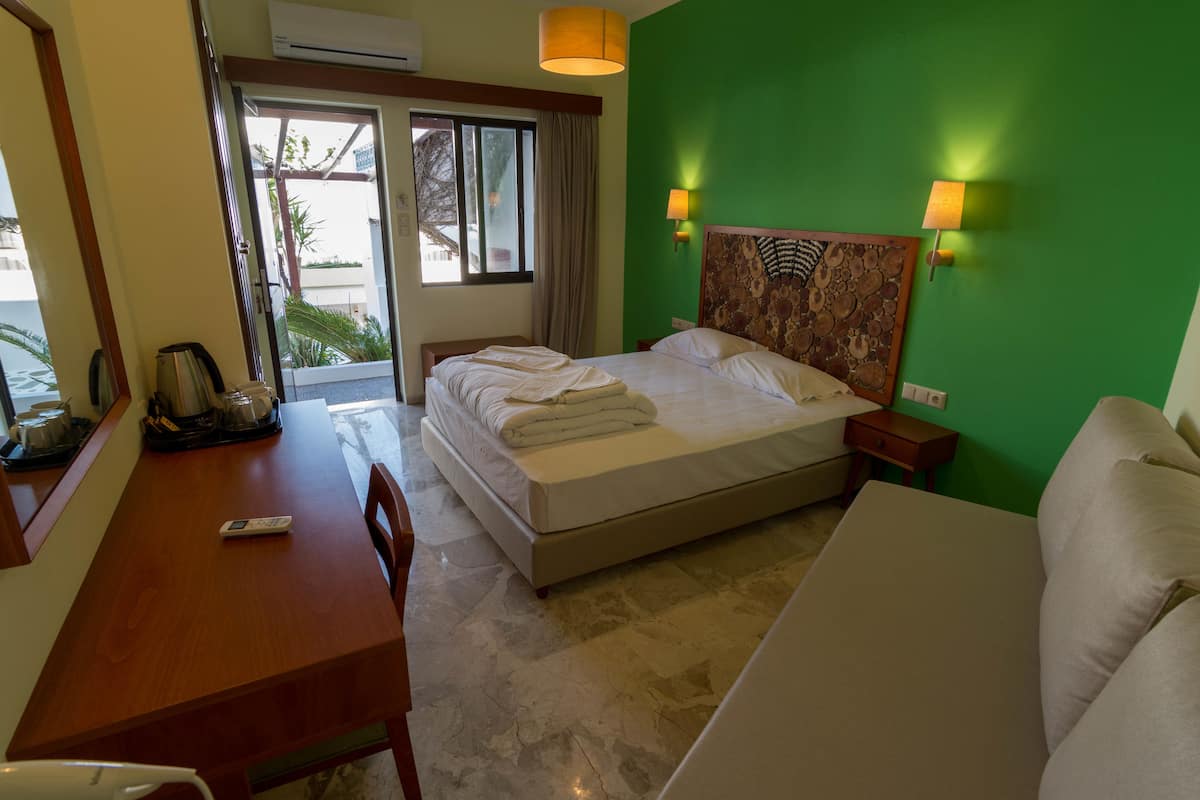 A hotel room with a bed, a desk, a chair, a sofa, and a window with curtains.