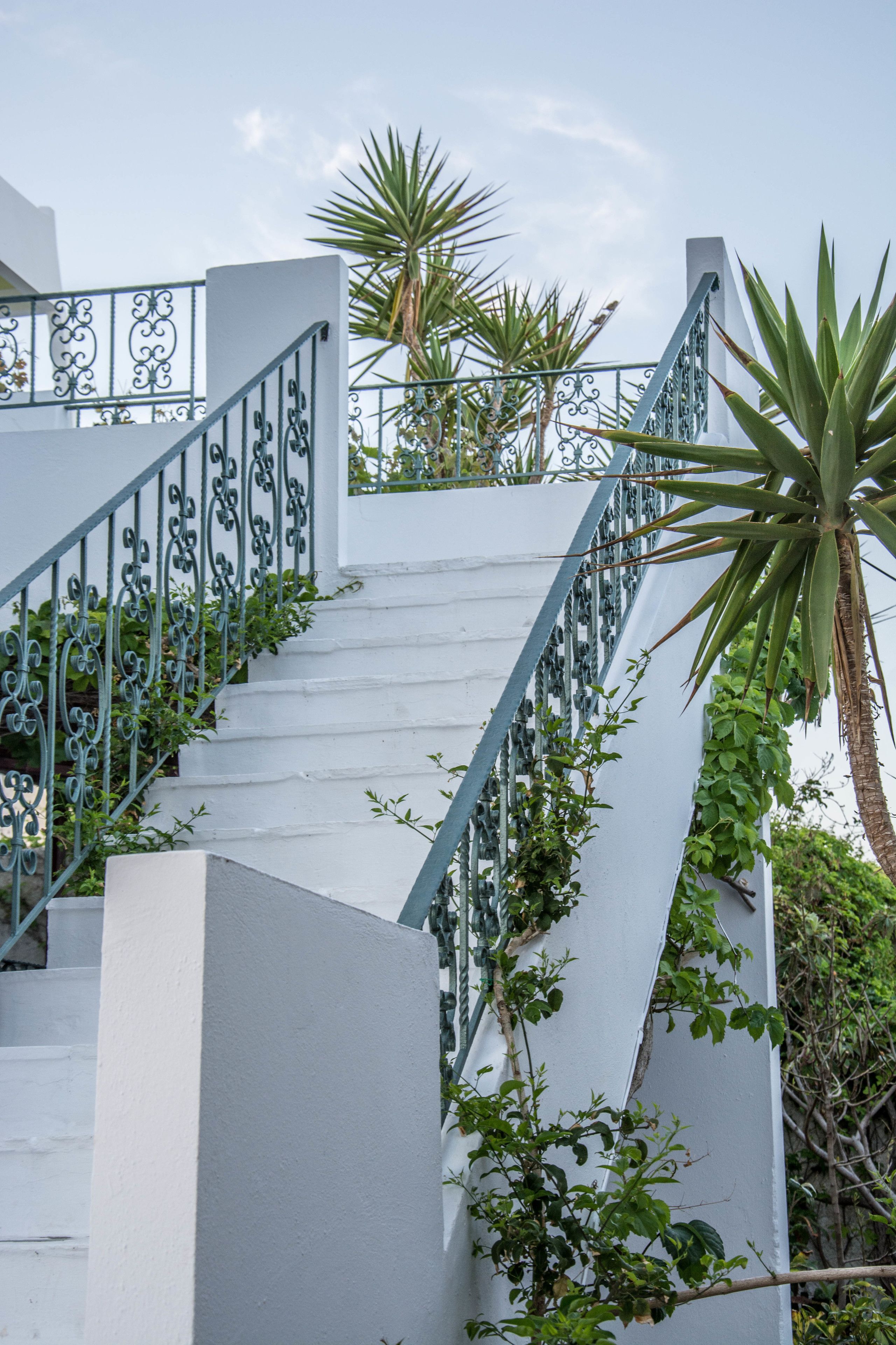 Een trap met witte muren en groene leuningen, die leidt naar een balkon met planten.