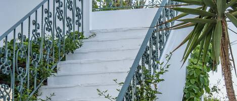 Een trap met witte muren en groene leuningen, die leidt naar een balkon met planten.