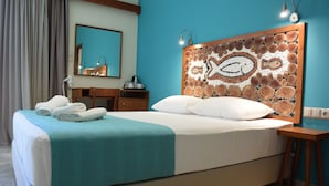 Un lit bien fait, recouvert d’une couverture turquoise, avec une tête de lit en bois ornée d’un motif de poisson, une table de chevet en bois et un miroir au-dessus de la commode.