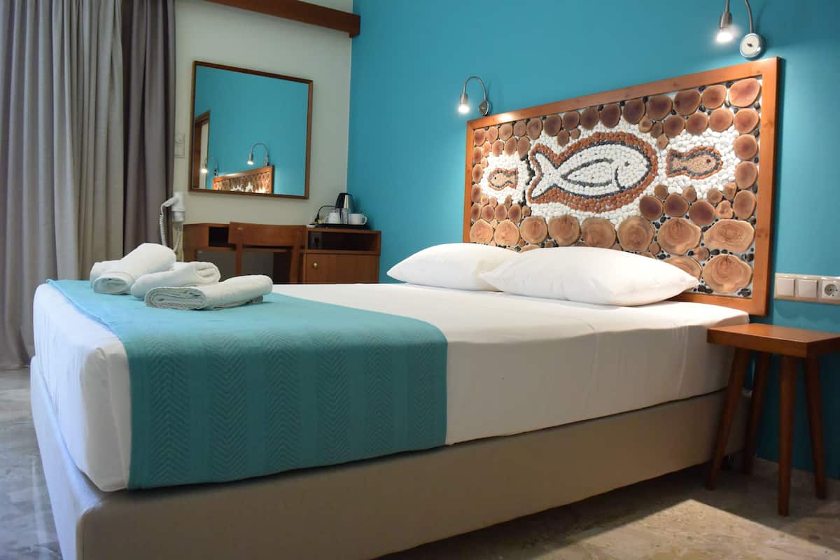 A neatly made bed with a teal blanket, a wooden headboard with a fish design, a wooden nightstand, and a mirror above the dresser.