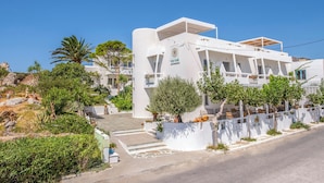 Un bâtiment moderne, de couleur blanche, doté d’un toit plat, d’un espace extérieur couvert aménagé en coin salon et d’un jardin paysager avec des arbres et des arbustes.
