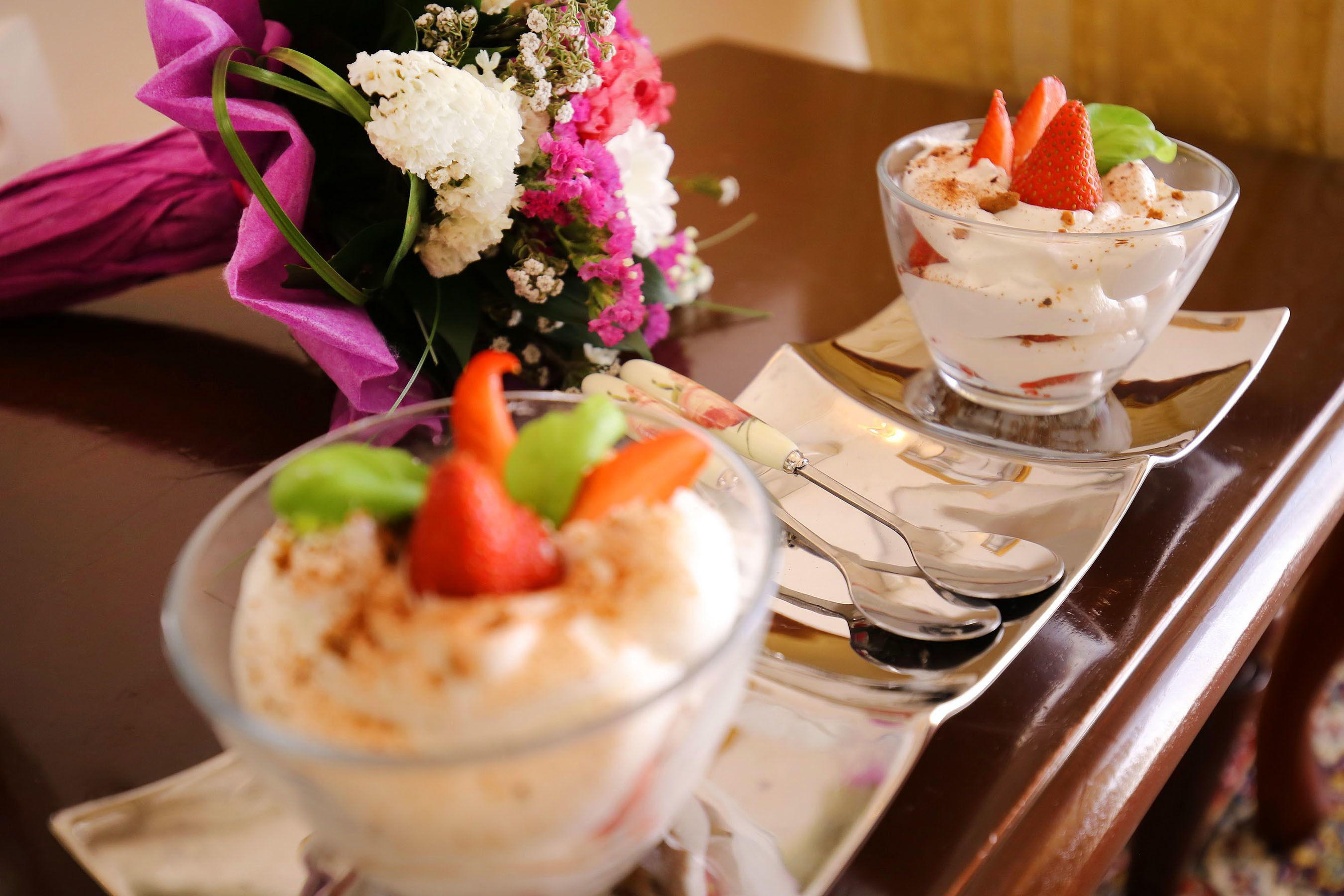 Dos tazones de postre sobre una bandeja con un ramo de flores al fondo.