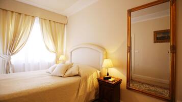Una habitación de hotel con una cama grande, una mesita de noche con lámpara, un espejo y una ventana con cortinas.
