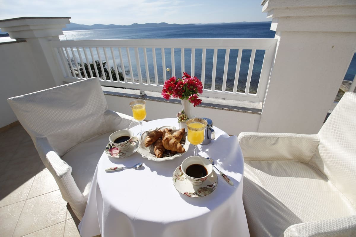 A table set with croissants, coffee, and orange juice on a balcony with a view of the sea.