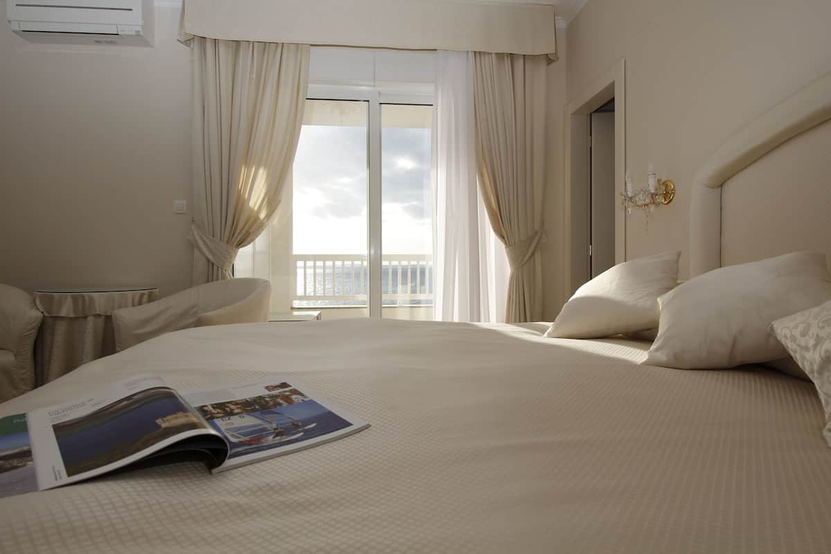 A hotel room with a large bed, a window with curtains, a bedside table, and a magazine on the bed.