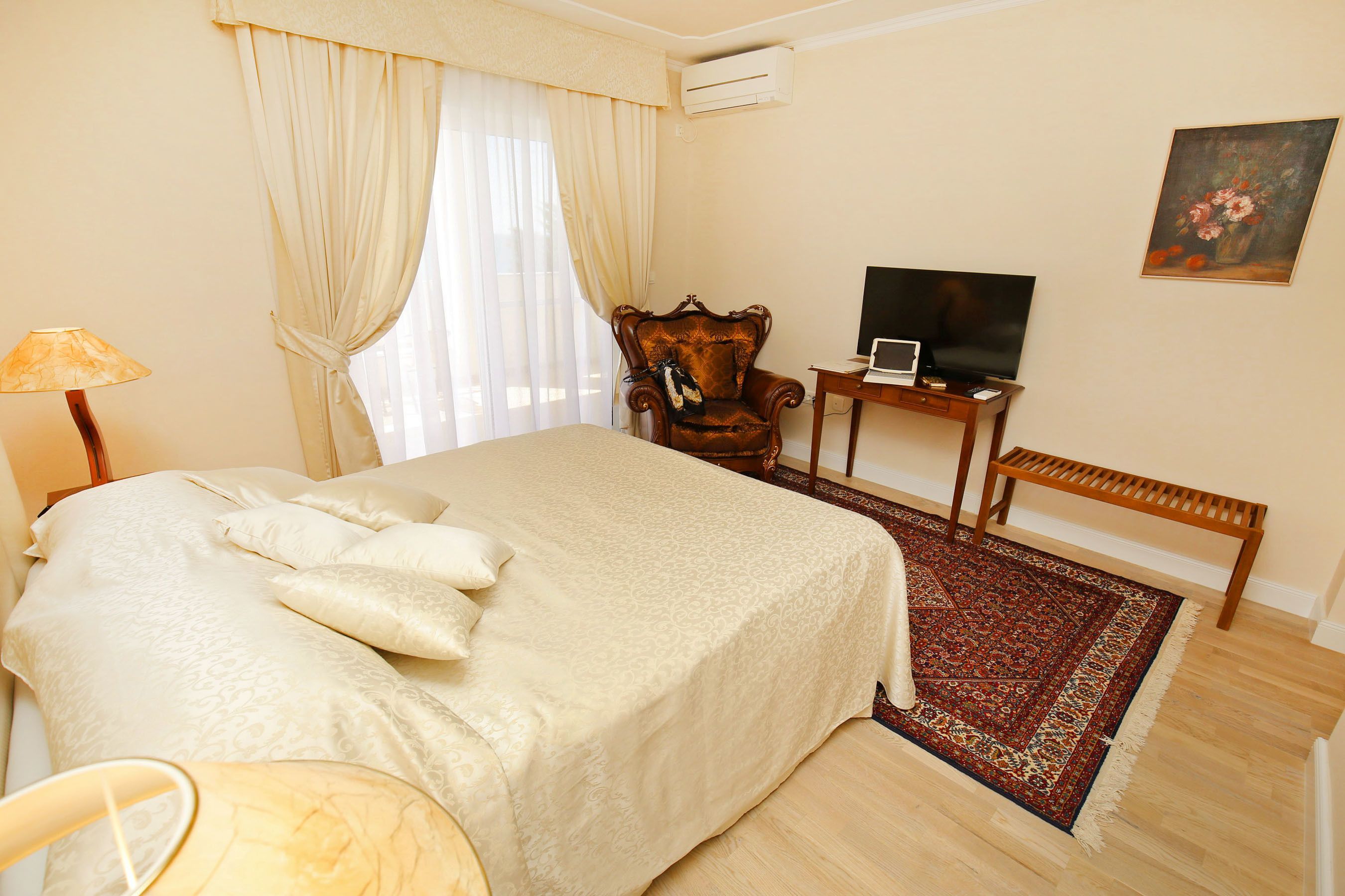 A bedroom with a bed, a chair, a table with a TV, and a painting on the wall.