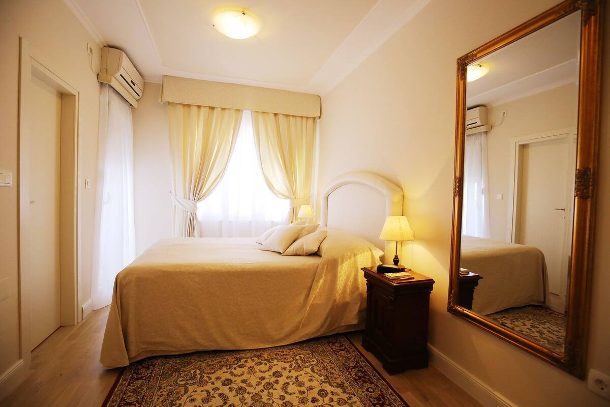 A hotel room with a bed, a nightstand, a mirror, and a window with curtains.