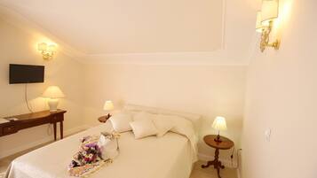 A neatly made bed with a floral arrangement, bedside lamps, a flat-screen TV, and a small table with a lamp.