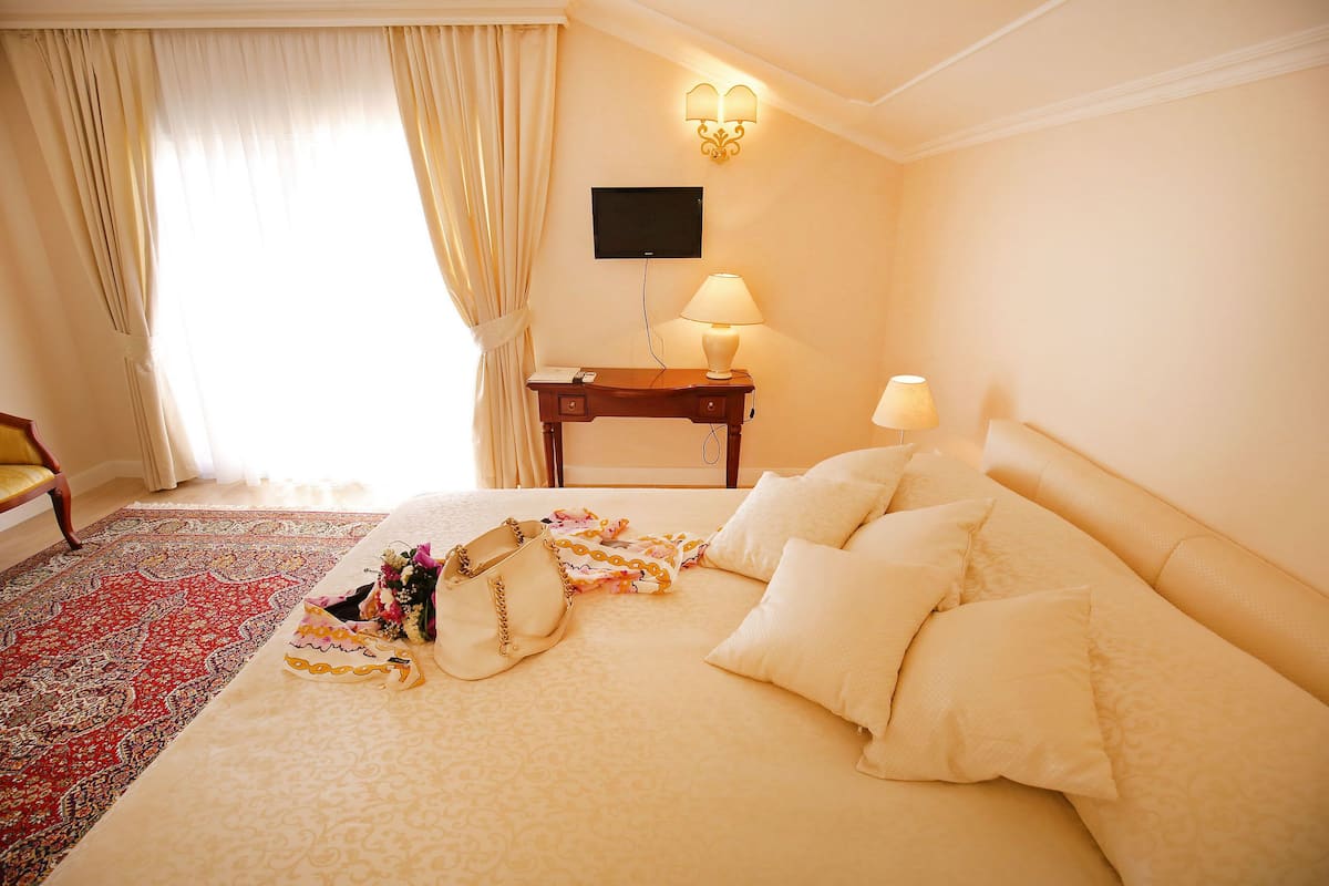 A hotel room with a large bed, a desk with a lamp, a television, and a red patterned rug.