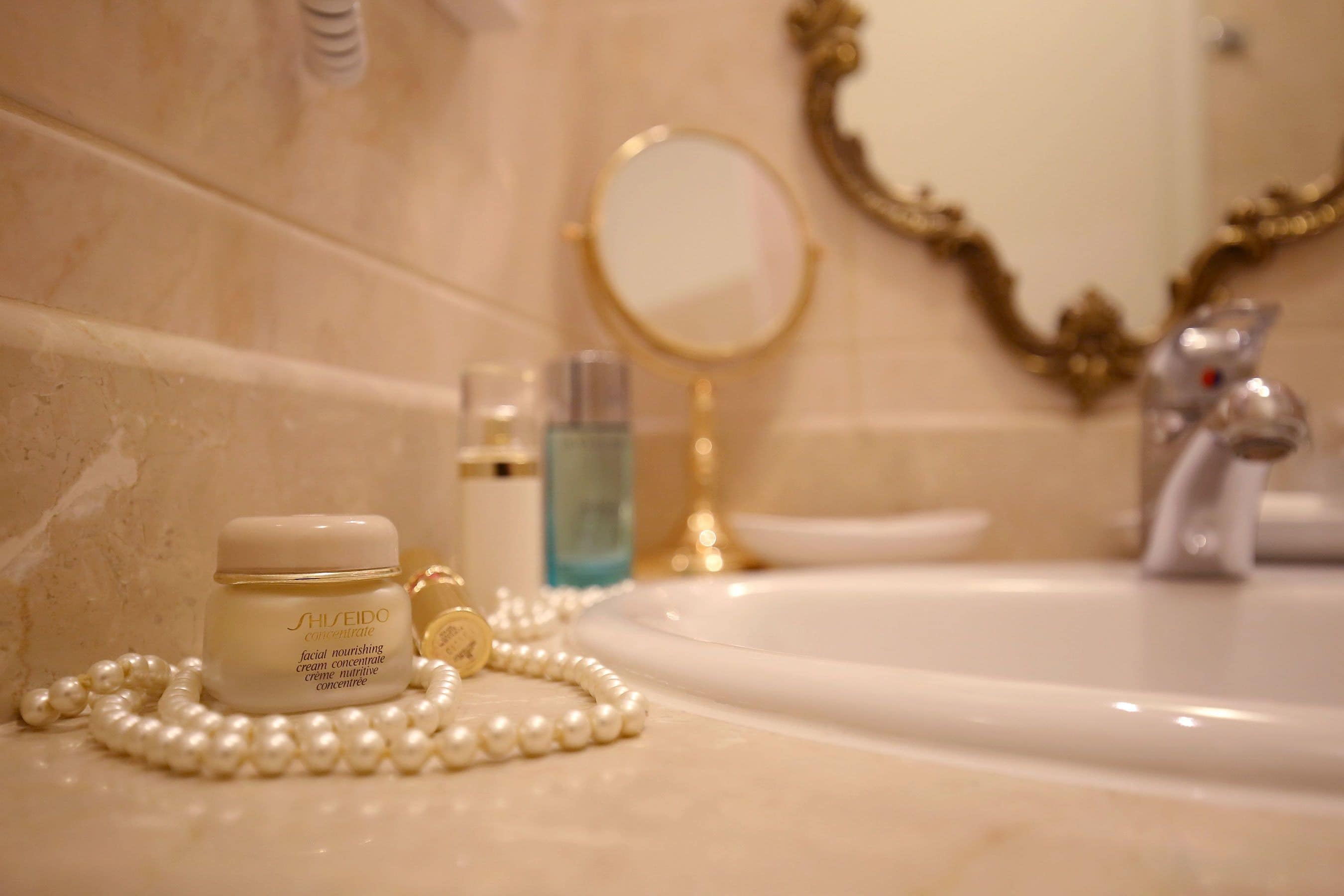 A bathroom vanity with a white sink, a gold-framed mirror, and a jar of cream.